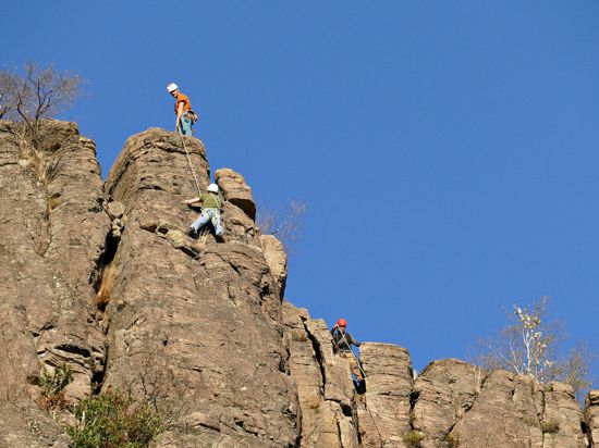Ein Kletterer seilt einen zweiten Kletterer an einer Felswand ab.