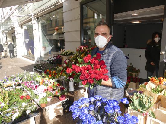 Ein Mann steht vor seinem Blumengeschäft und hat Blumen in der Hand. 