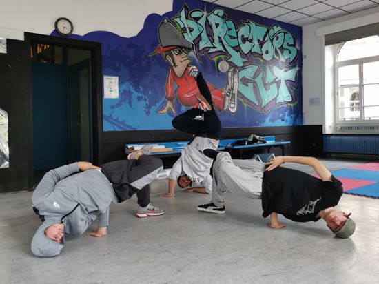 Drei Breakdancer machen eine akrobatische Figur vor einer Graffiti-Wand.