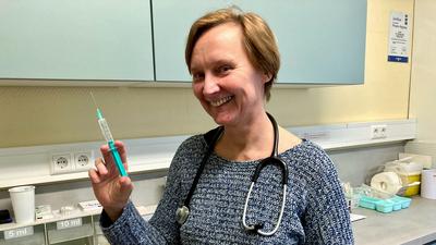 Eine Frau steht in einem medizinischen Labor und hält eine Spritze in der Hand.
