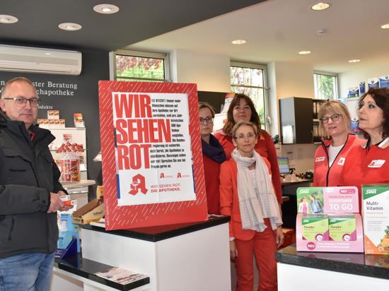 Rot gekleidete Angestellte in der Rebland-Apotheke neben einem Schild mit der Aufschrift „Wir sehen rot“.