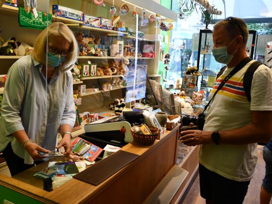 Ein Tourist mit Kamera um den Hals zückt seinen Geldbeutel. Die Verkäuferin wickelt seine Einkäufe ein.