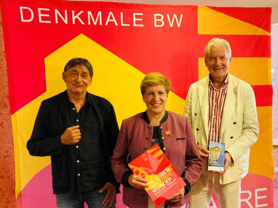 Bau-Ministerin Nicole Razavi steht mit Claus Wolf (links) und Oberbürgermeister Dietmar Späth für einem Transparent mit der Aufschrift „Denkmale BW“.