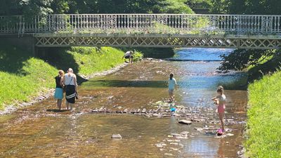 Spaß im seichten Wasser: Manche Fußgänger nutzen die Gelegenheit, die Füße in der sanft dahinplätschernden Oos zu kühlen