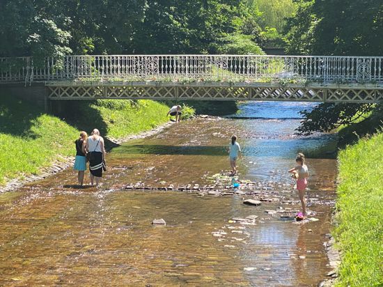 Spaß im seichten Wasser: Manche Fußgänger nutzen die Gelegenheit, die Füße in der sanft dahinplätschernden Oos zu kühlen