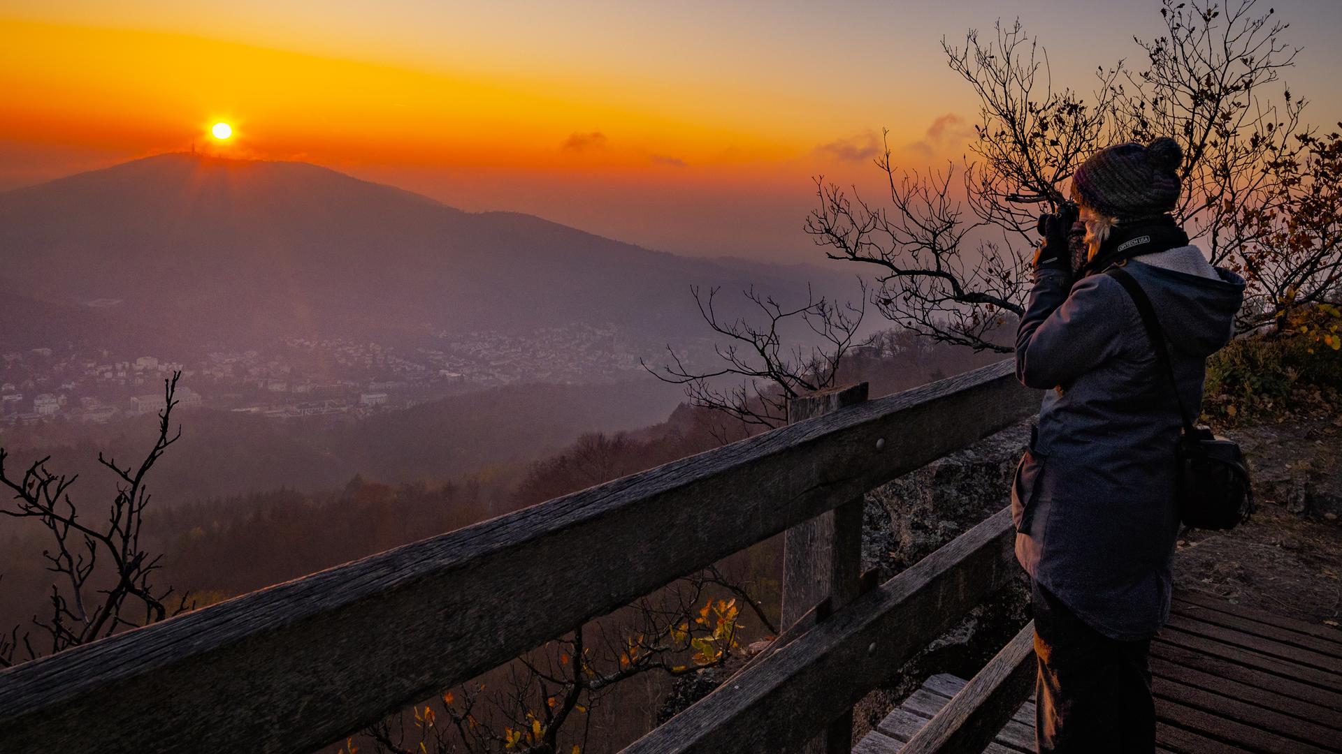 Eine Frau steht auf einer Aussichtsplattform und blickt in den Sonnenuntergang.