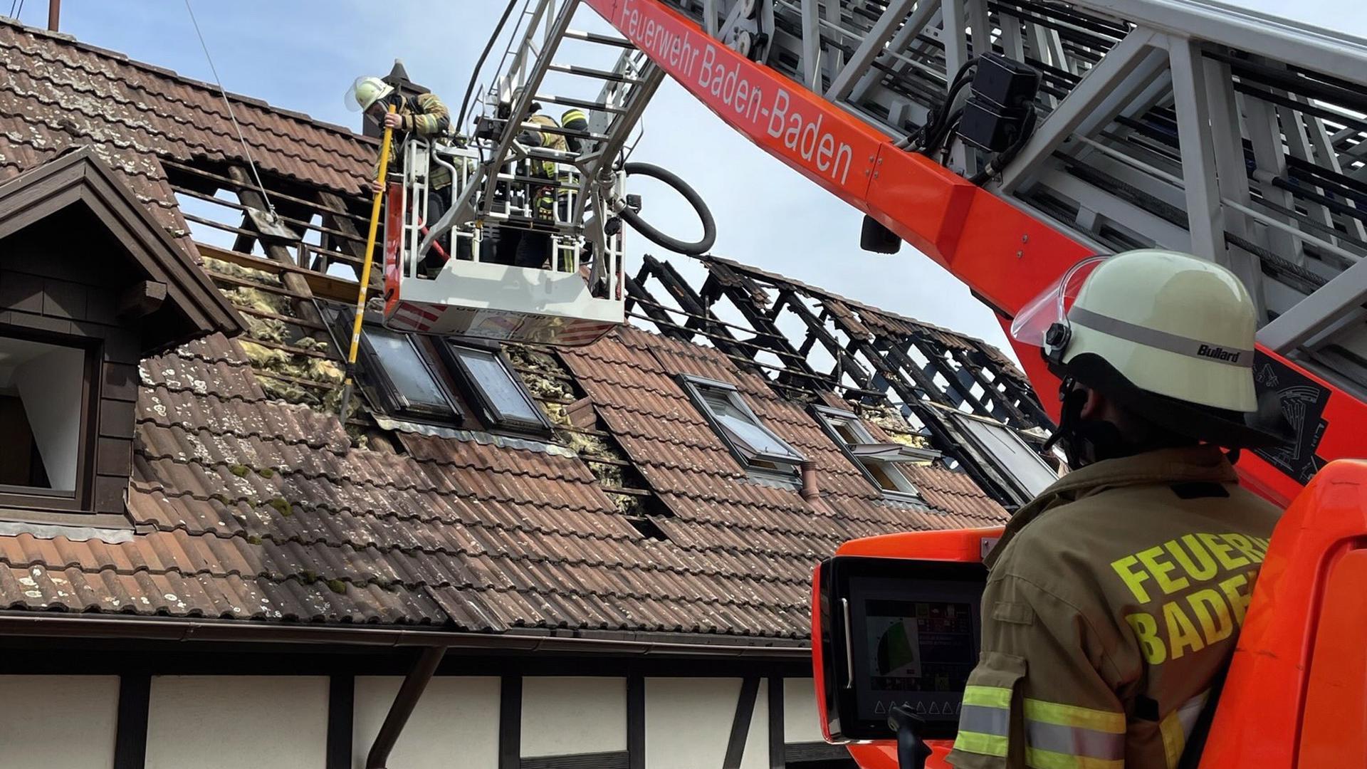 Ein Feuerwehrmann der Baden-Badener Feuerwehr entfernt von einer Drehleiter aus verkohlte Teile aus dem Dachstuhl eines Gebäudes in der Ooser Burgstraße.