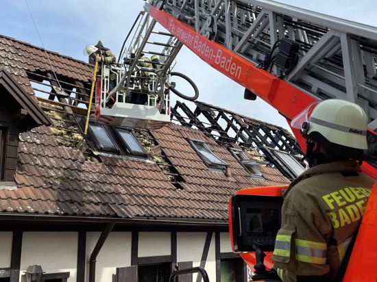 Ein Feuerwehrmann der Baden-Badener Feuerwehr entfernt von einer Drehleiter aus verkohlte Teile aus dem Dachstuhl eines Gebäudes in der Ooser Burgstraße.