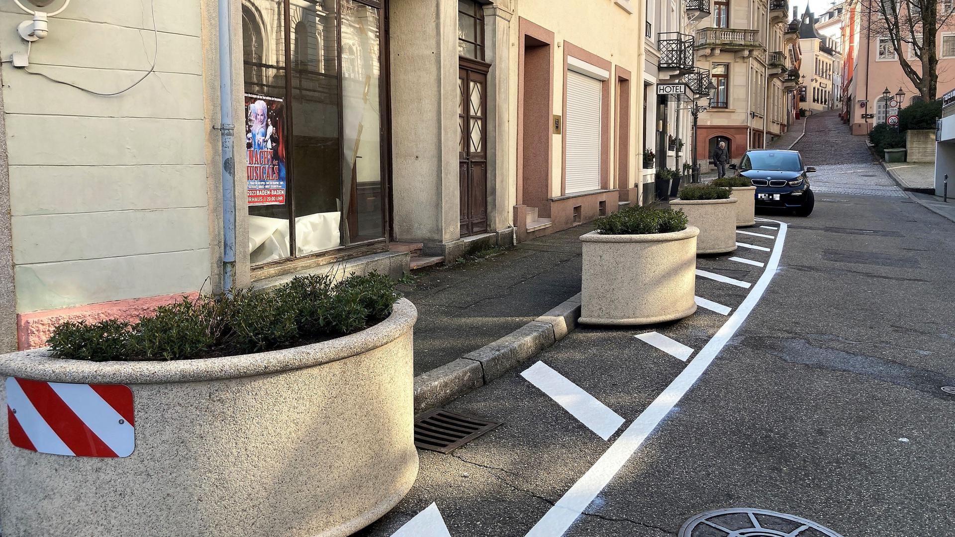 Auf einer Straße mit weißen Markierungslinien stehen Pflanzkübel.