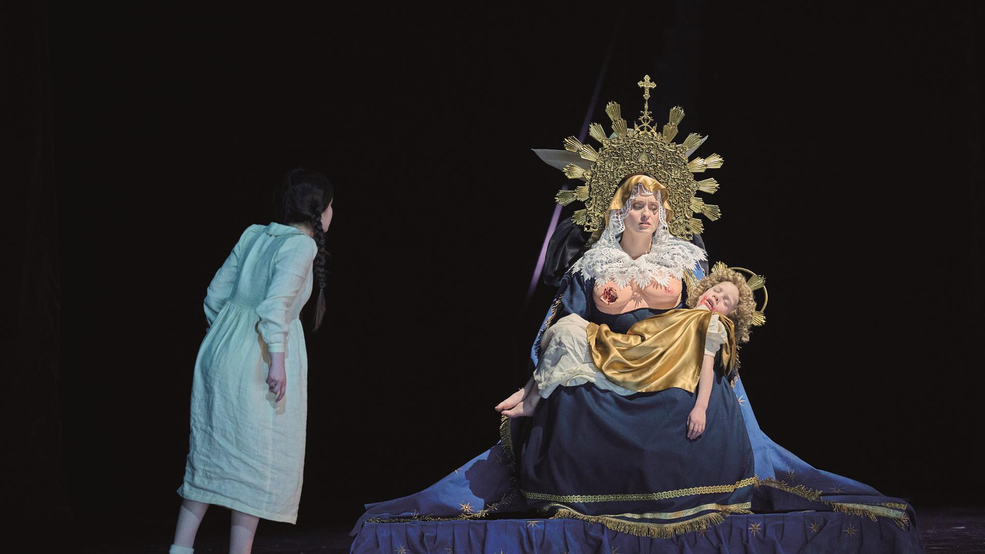 Ein Mädchen (Vivien Hartert) starrt auf eine Muttergottesfiggur mit zerbissener Brust in einer Szene aus der Oper „Die Frau ohne Schatten“ bei den Osterfestspielen 2023 in Baden-Baden in der Regie von Lydia Steier.