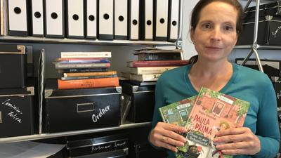 Die Drehbuchautorin Regine Bielefeldt steht vor einem Regal voller Ordner, sie hält ihre Kinderbücher in der Hand.