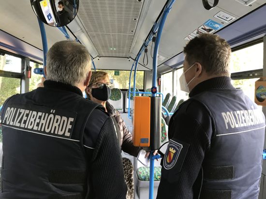 Zwei Männer der Polizeibehörde reden mit einer Frau, die eine Maske trägt, in einem Bus in Baden-Baden