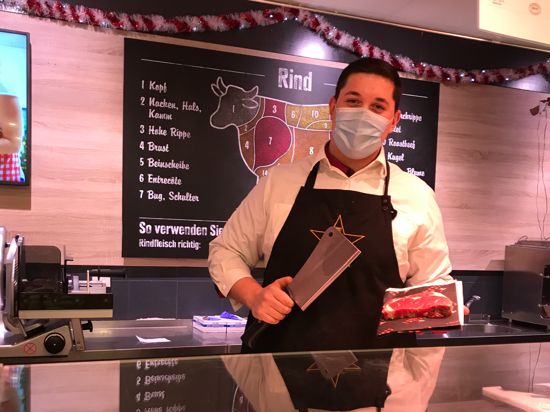 Der Fleischereifachverkäufer Adrian Stanciu hält ein Messer und ein Stück Fleisch in der Hand. 