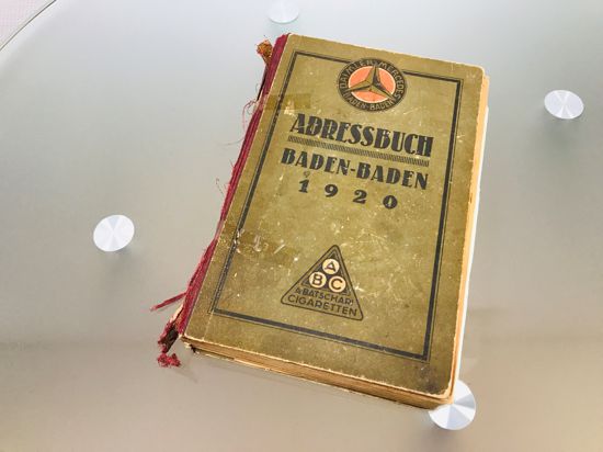 Ein Adressbuch von Baden-Baden aus dem Jahr 1920 liegt auf einem Glastisch.