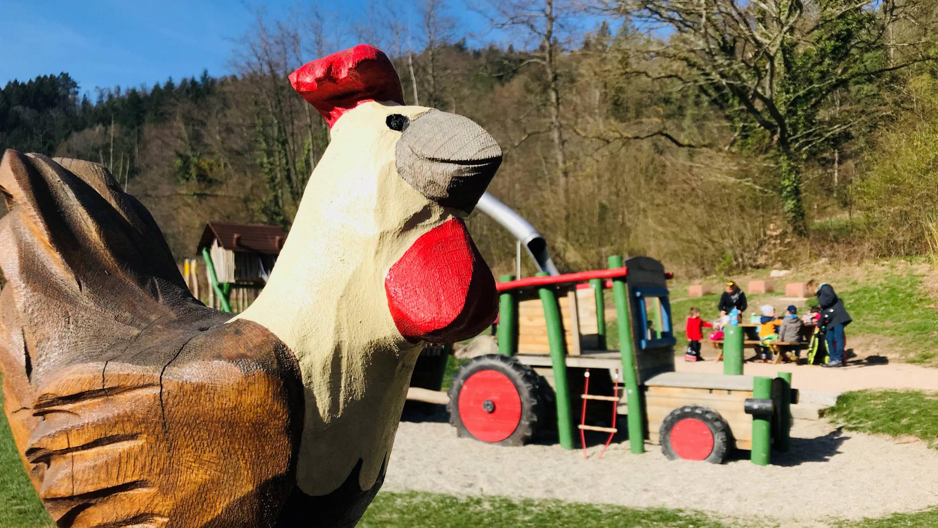 Am Spielplatz Sägmüllermatte in Baden-Baden  geht es um das Thema Bauernhof. Zu sehen sind ein großes hölzernes Huhn und ein Spielgerät, das auf einem Traktor basiert. 