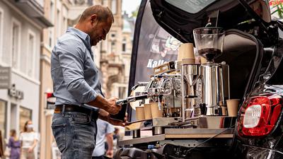 Ein Mann arbeitet an einer Espresso-Maschine, die im Kofferraum eines Smarts installiert ist.