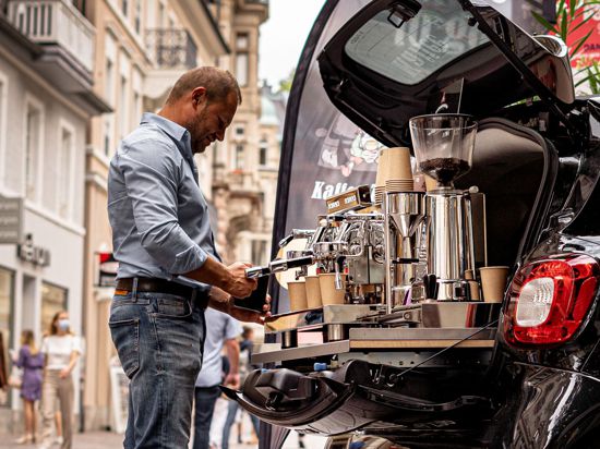 Ein Mann arbeitet an einer Espresso-Maschine, die im Kofferraum eines Smarts installiert ist.