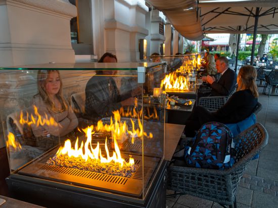 Mehrere Kaminöfen brennen zwischen den Tischen auf der Außenterrasse eines Restaurants.