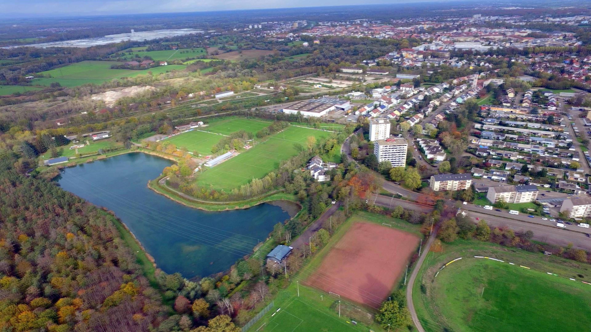 Mehrere Sportplätze und ein Waldstück grenzen an einen See an.