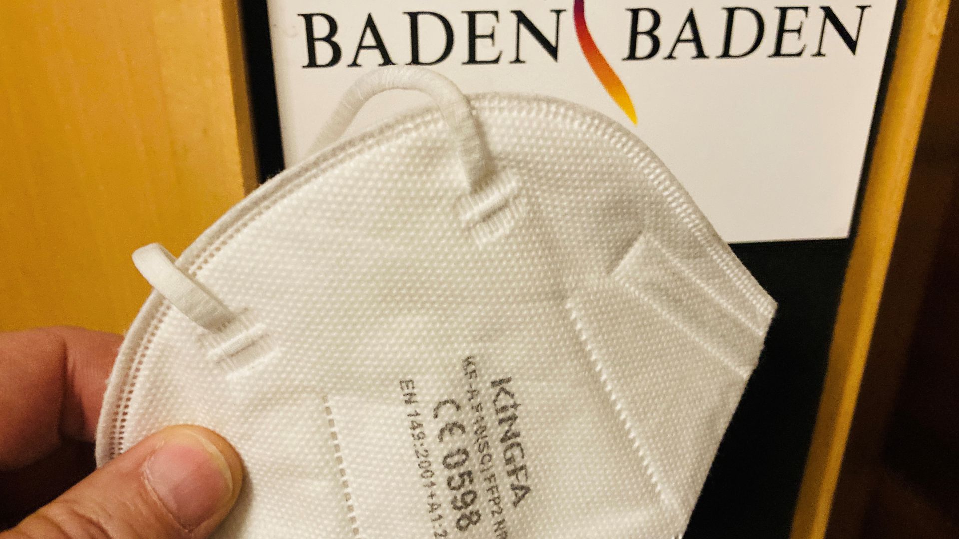 EVor einem Pult mit der Aufschrift „Baden-Baden“ wird eine Mund-Nasen-Maske gehalten. 