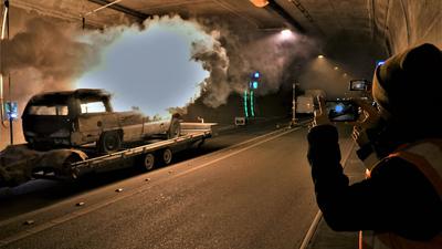 In einem Tunnel brennt ein Autowrack. Menschen halten das Ereignis mit ihren Handys fest.
