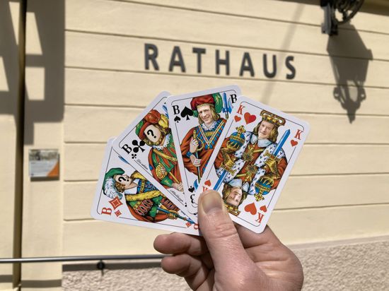 Eine Hand hält Skatkarten mit drei Buben und einem König vor dem Baden-Badener Rathaus. Auf den König ist das Gesicht von OB Dietmar Späth montiert, auf einen Bube das von Bürgermeister Roland Kaiser.