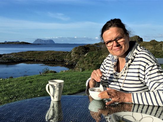 Eine Frau sitzt mit einer Kaffeetasse in der Hand auf einer Terrasse einer Insel in Norwegen