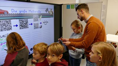 Kinder und ein Erwachsener an einem Whiteboard, auf dem QR-Codes zu sehen sind