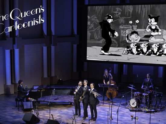 Musiker stehen auf der Bühne, im Hintergrund läuft auf einer Leinwand ein Zeichentrickfilm. 