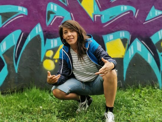 Frau sitzt in der Hocke vor einer Graffiti Wand.