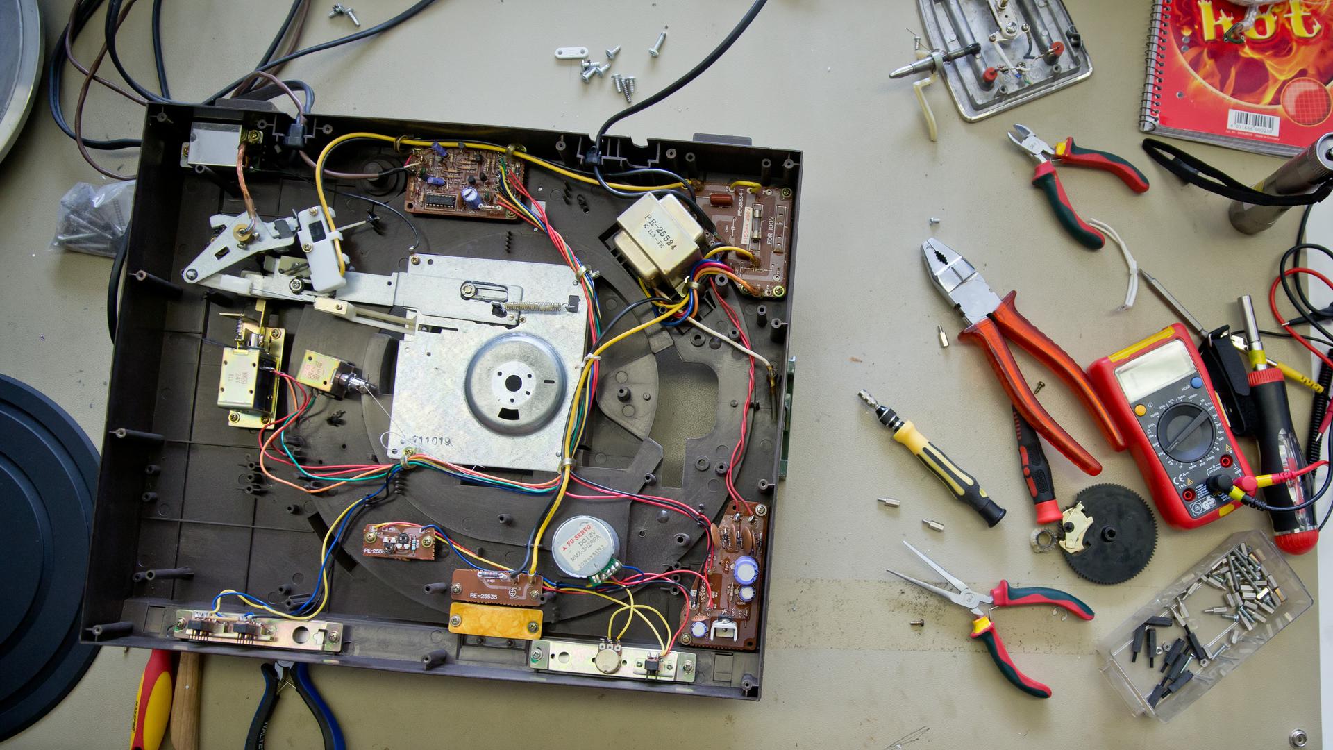 Ein defekter und geöffneter Schallplattenspieler liegt im Repair Café zur Reparatur neben Werkzeugen auf einem Tisch.