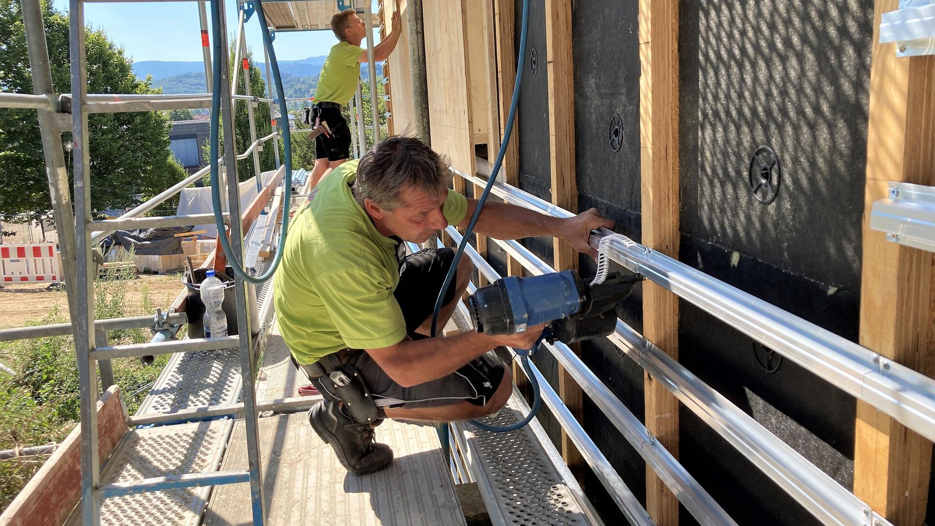 Handwerker schrauben Metallträger an eine Gebäudefassade.