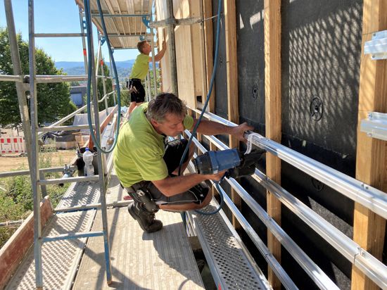 Handwerker schrauben Metallträger an eine Gebäudefassade.