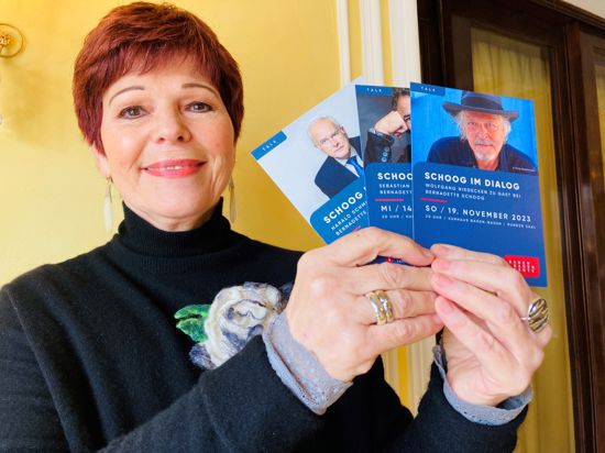 Moderatorin Bernadette Schoog hält Werbe-Karten für ihre Reihe „Schoog im Dialog“ in der Hand. 