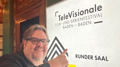 Urs Spörri, künstlerischer Leiter des Fernsehfilm- und Serienfestivals Televisionale, steht vor einem Display mit der Aufschrift „Televisionale“. 