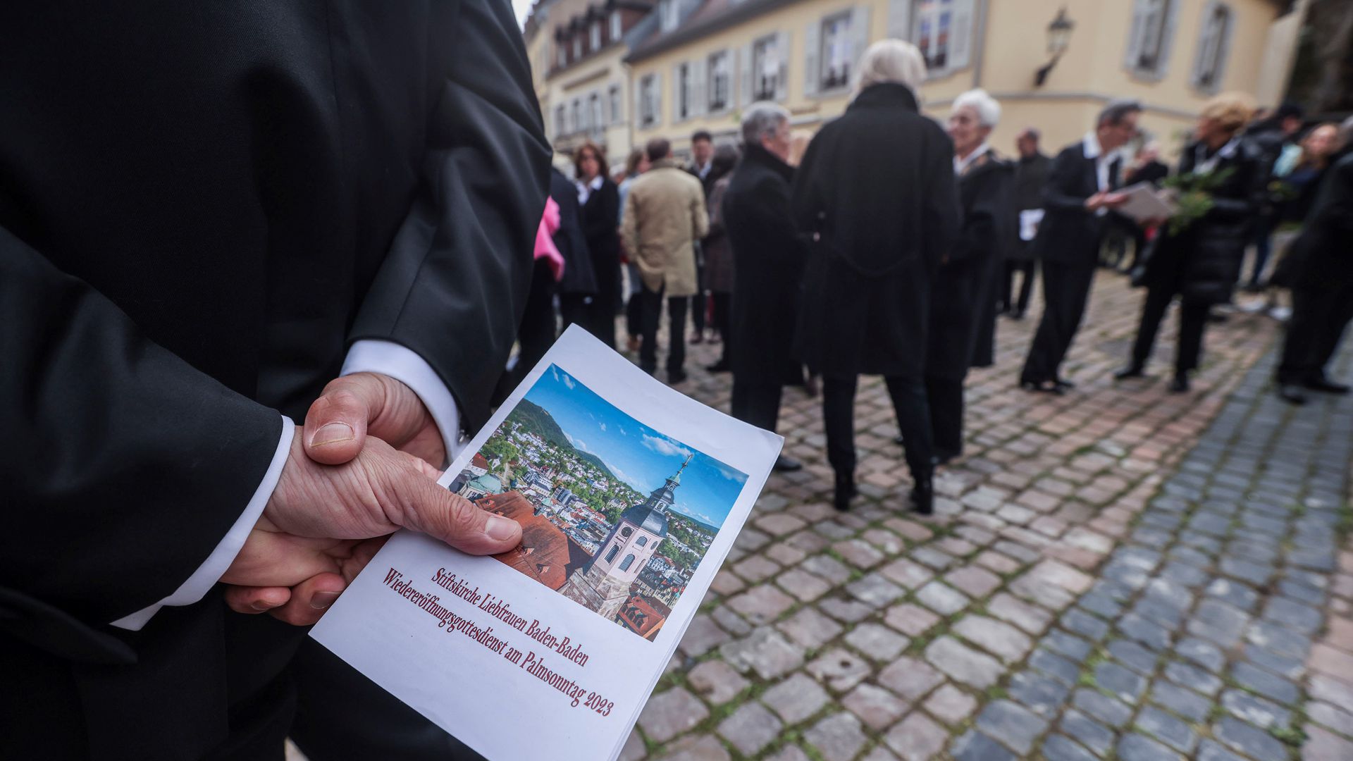 Vor der Stiftskirche hält ein Teilnehmer am Gottesdienst zur Wiedereröffnung einen Flyer zum großen Ereignis in der Hand. 