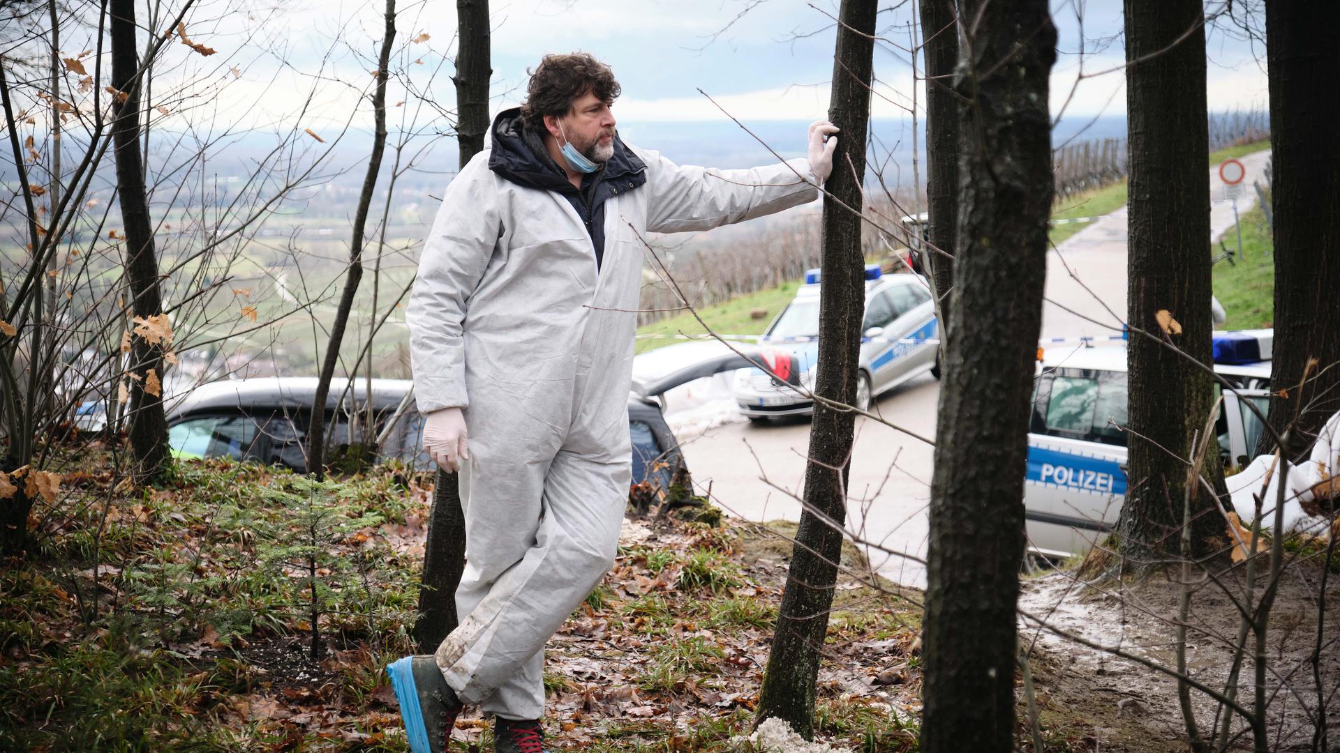 Schauspieler Hans-Jochen Wagner steht Dreharbeiten zum Schwarzwald-Tatort "Das Geständnis" in einem weißen Schutzanzug im Wald.
