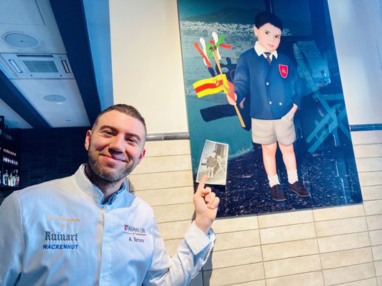 Der Koch Angelo Tortora steht im Restaurant „87 Mamma Lina“ in Baden-Baden vor einem Bild, das seinen Vater Carmine als Schulanfänger zeigt. 