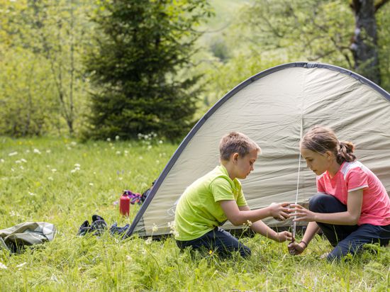 Zwei Kinder spielen auf einer Wiese vor einem Zelt, das in einem Trekkingcamp im Nordschwarzwald aufgebaut ist. 