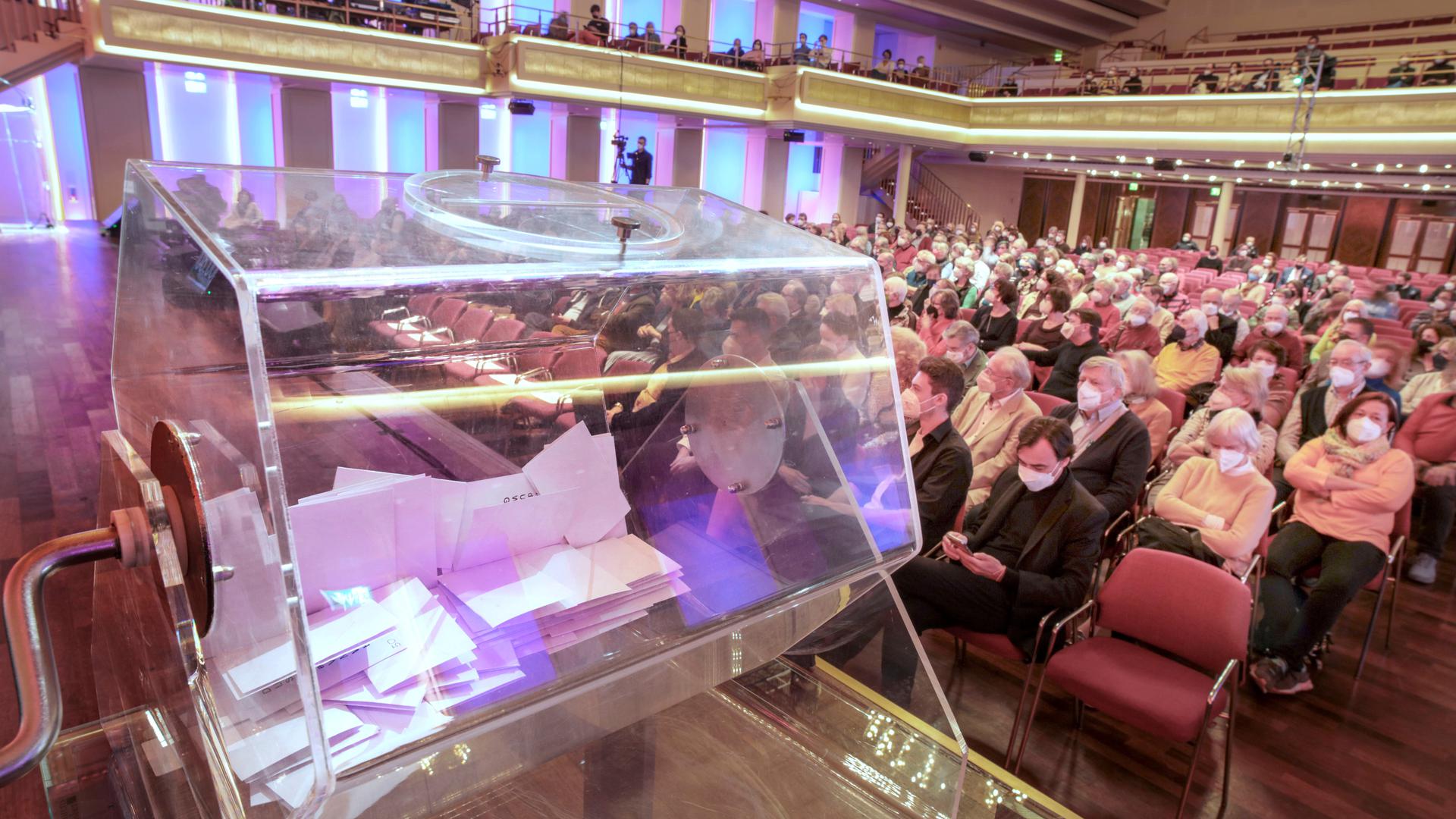 Auf der Bühne des Bénazet-Saals im Kurhaus steht eine Glastrommel mit Zuschriften. Im Saal verfolgen Besucher die Kandidaten-Vorstellung.