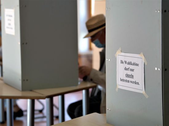 Ein Wähler mit Mund-Nasen-Schutzmaske sitzt in einer Wahlkabine. 