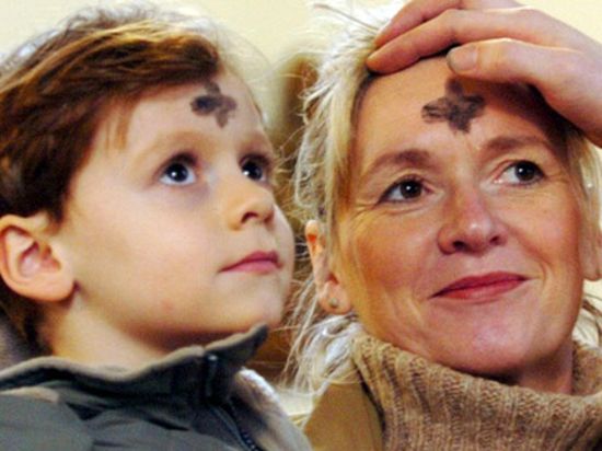 Ein Priester malt einer Frau und einem Kind ein Aschekreuz auf die Stirn.