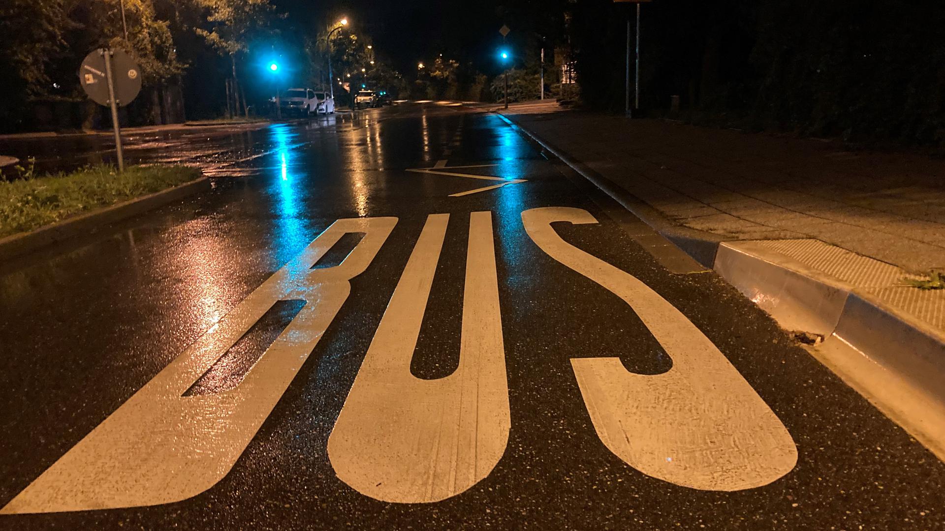 Schriftzug „Bus“ auf der regennassen Straße bei Nacht