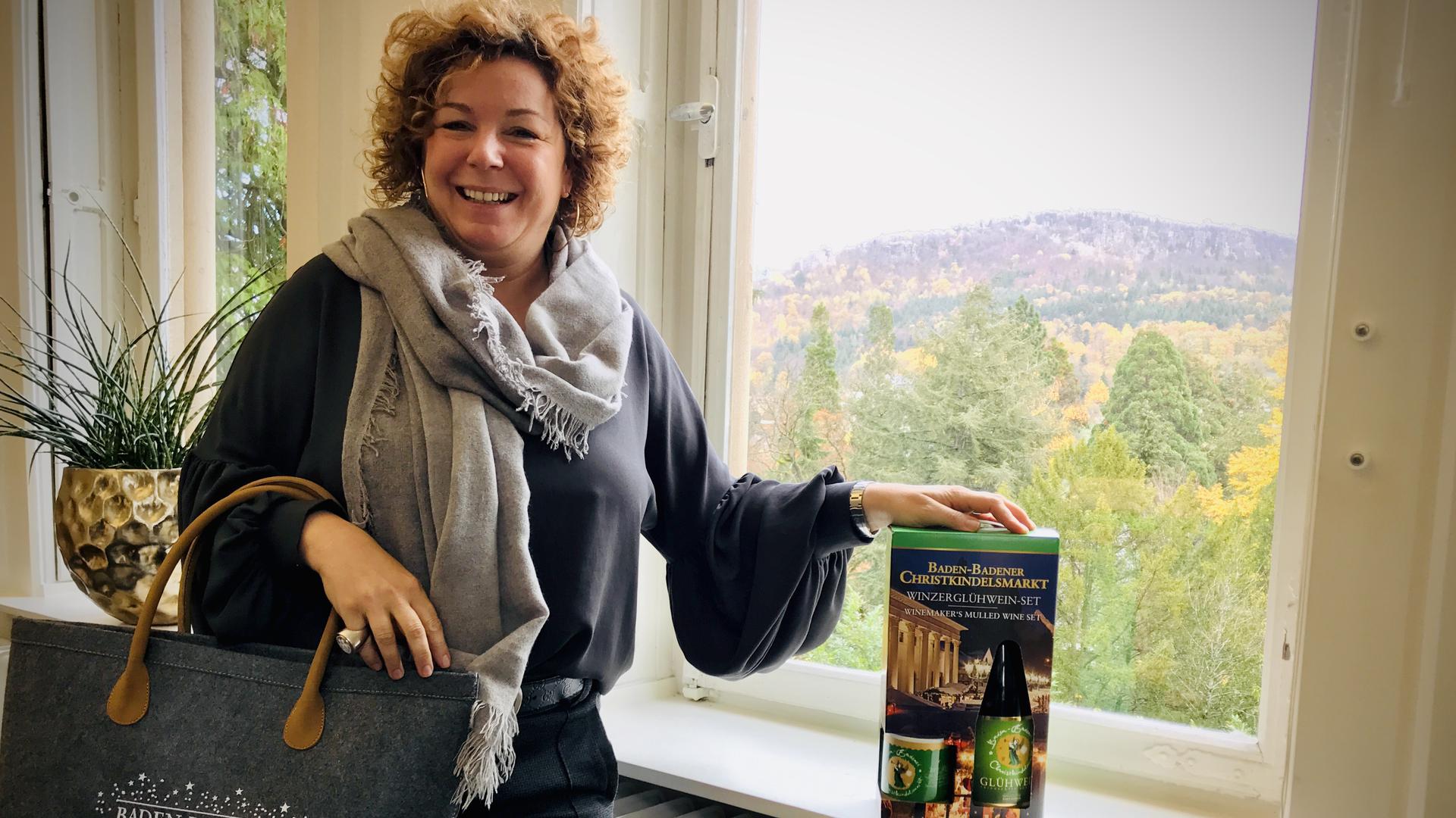Die Baden-Badener Tourismuschefin Nora Waggershauser zeigt eine Einkaufstasche mit Christkindelsmarkt-Aufdruck und ein Paket mit Winzer-Glühwein und Tasse. 
