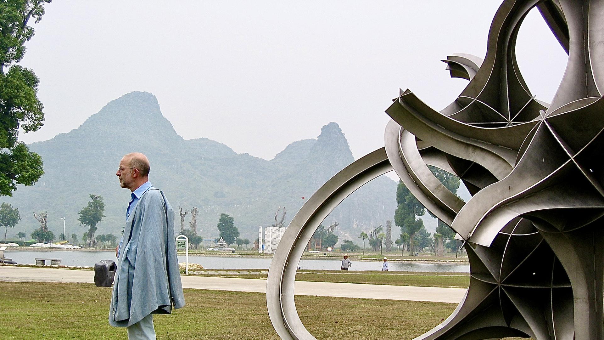 Eberhard Eckerle in der Landschaft von Guilin in China vor seiner Stahlskulptur „Strange Loops“ aus dem Jahr 2001