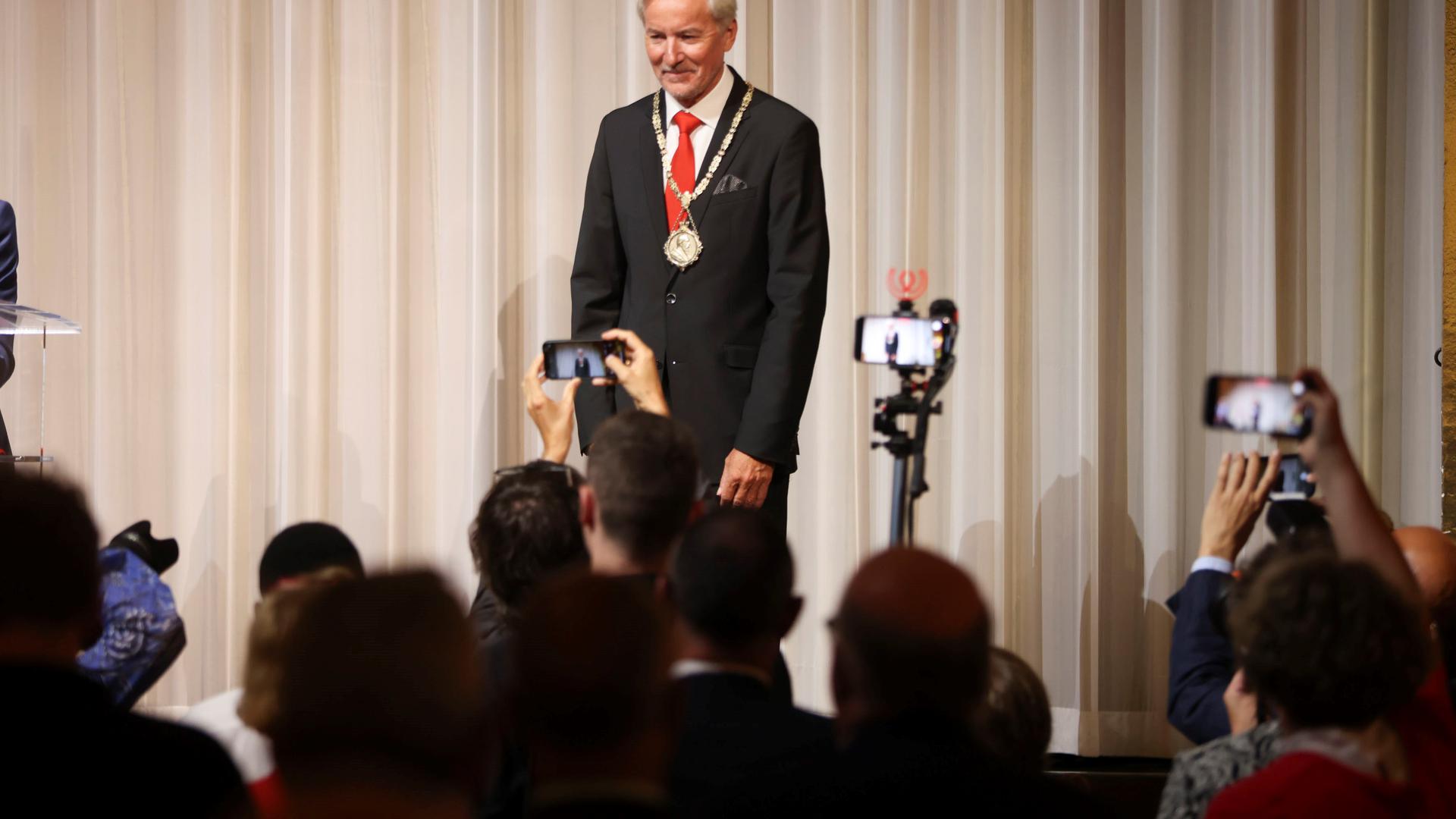 Oberbürgermeister Späth steht auf einer Bühne, lächelt und wird von vielen Personen fotografiert.