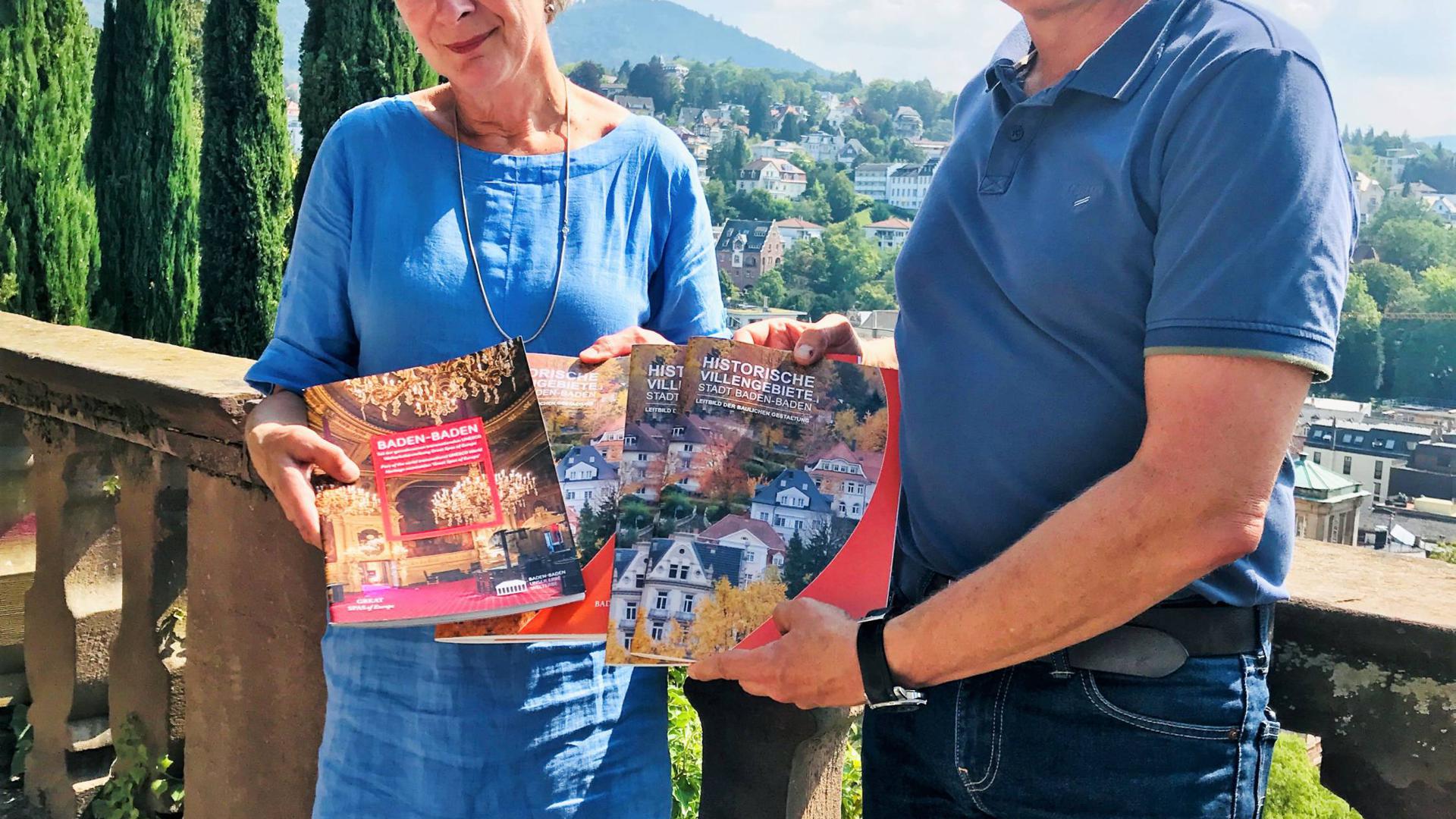 Die Baufibel und eine Broschüre zur Welterbe-Bewerbung zeigen Lisa Poetschki und Alexander Uhlig auf der Schlossbergterrasse – im Hintergrund das Villengebiet Annaberg.