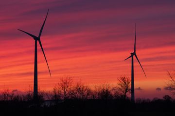 Windräder sind vor dem rötlich gefärbten Abendhimmel zu sehen.