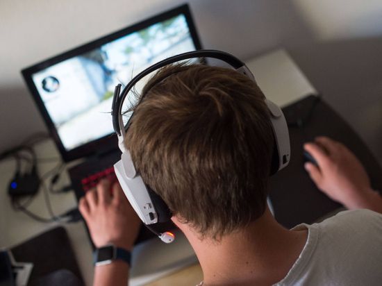 Ein junger Mann sitzt  mit einem Headset vor einem Laptop und spielt ein Online-Computerspiel.