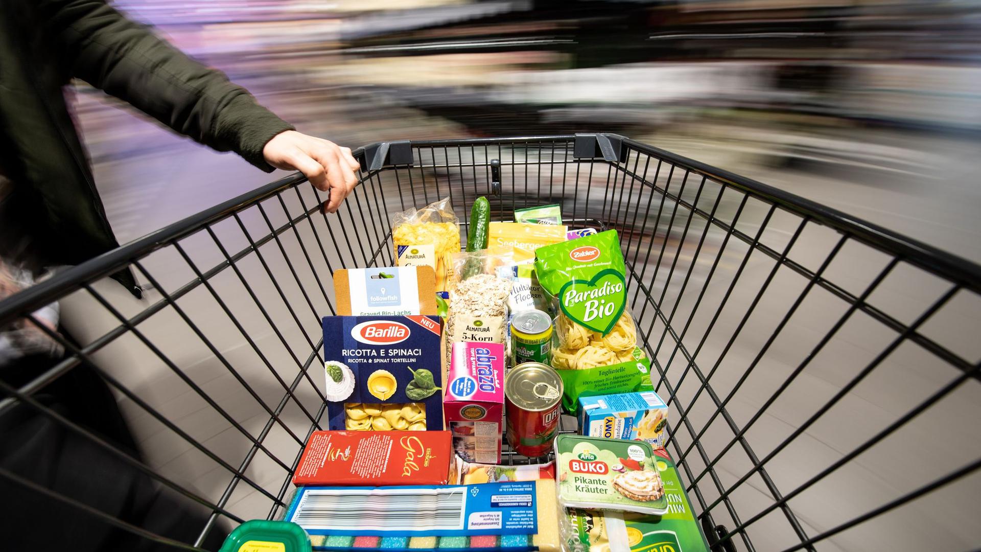 Ein Einkaufswagen wird durch einen Supermarkt geschoben. Die immer billiger werdenden Preise für Lebensmittel stehen in der Kritik.